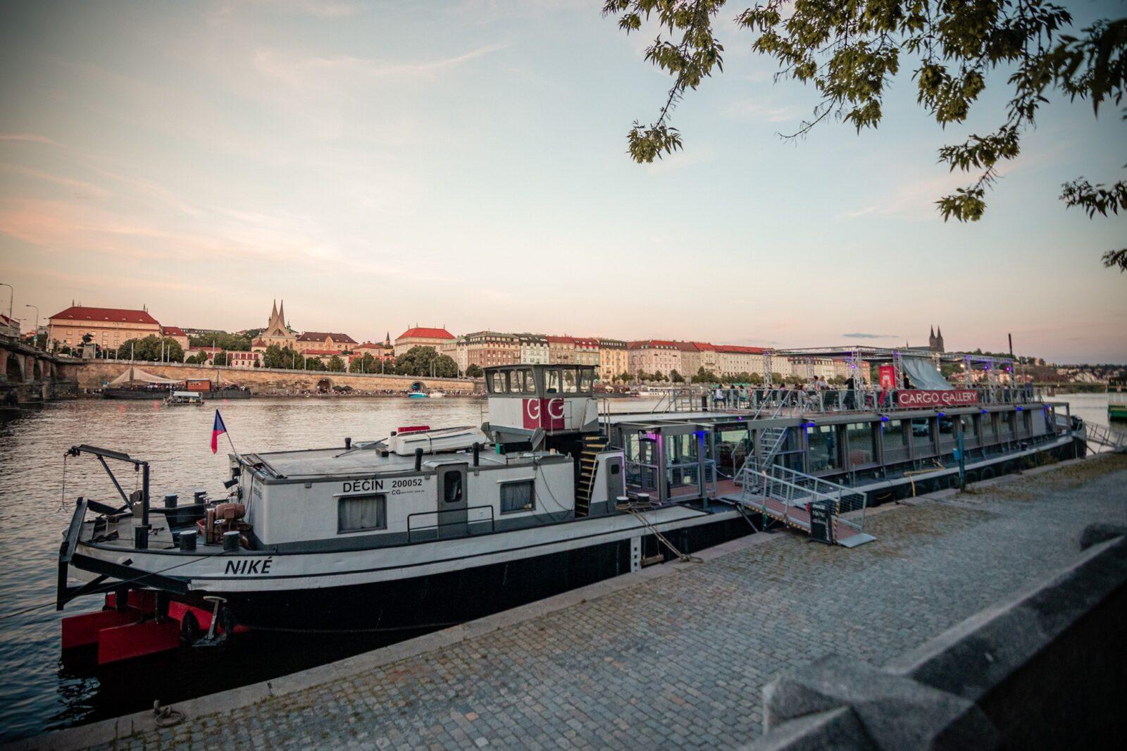 Cargo Gallery na pražské Náplavce při západu slunce — kontejnerová terasa u Vltavy, v záběru i zakotvená loď u nábřeží