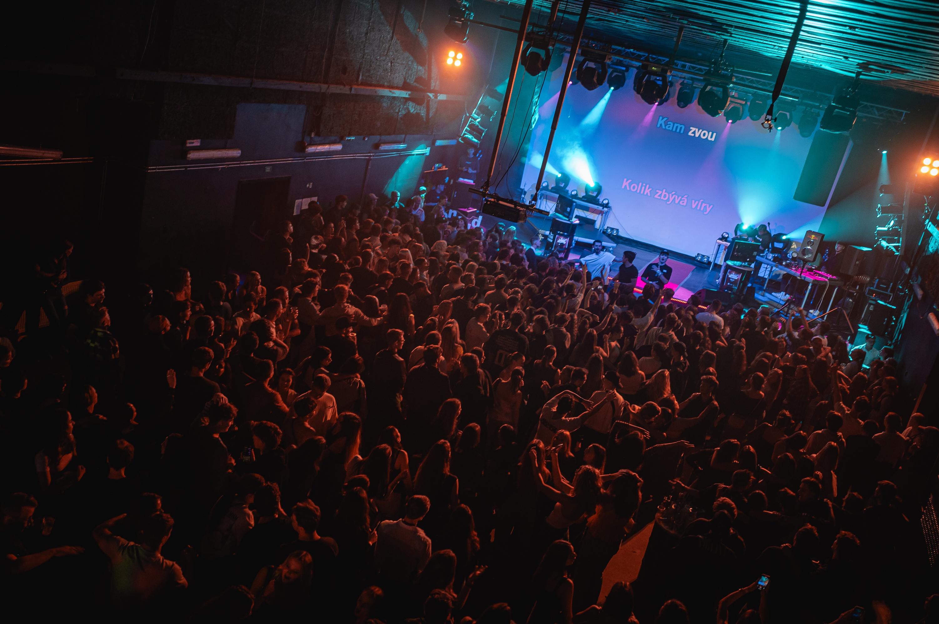 Široký záběr klubového sálu Karaoke Party v Olomouci s davem, tyrkysovými reflektory a velkou projekční obrazovkou